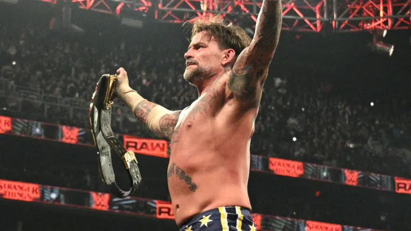 CM Punk Celebrates World Heavyweight Championship Retention on Monday Night Raw - TJR WRESTLING Professional wrestler CM Punk holds up the World Heavyweight Championship belt and raises his other hand in the air while standing in a wrestling ring on WWE Raw.
