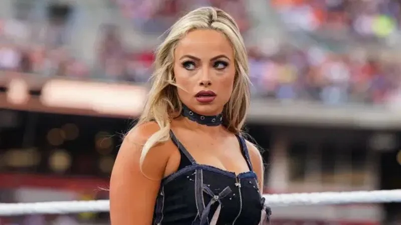 WWE women’s division star standing inside the ring during a live event, wearing black ring gear and looking toward the crowd.