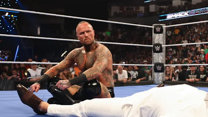 Aleister Black sits in the WWE ring during a SmackDown match, looking toward his opponent.