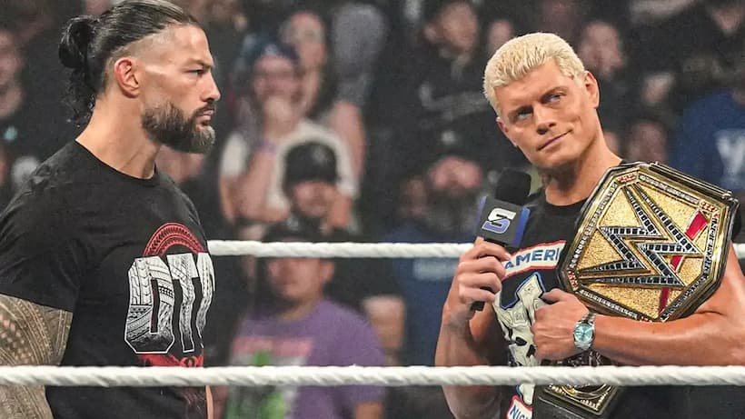 Two WWE Superstars face off in the ring as one holds a championship belt and speaks into a microphone.