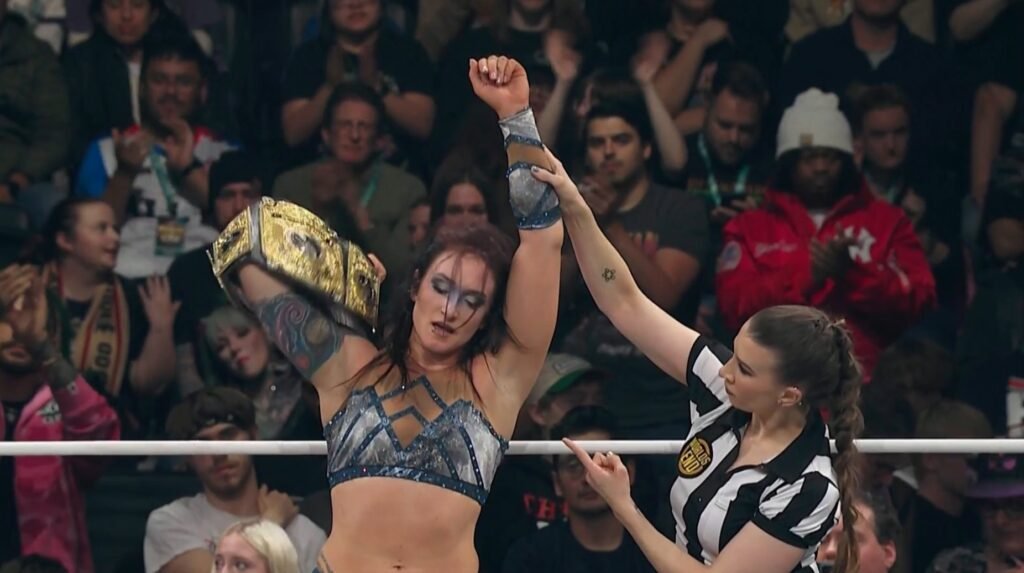 Kris Statlander celebrates her victory in an AEW ring, holding the AEW Women's World Championship over her shoulder as a referee raises her arm.
