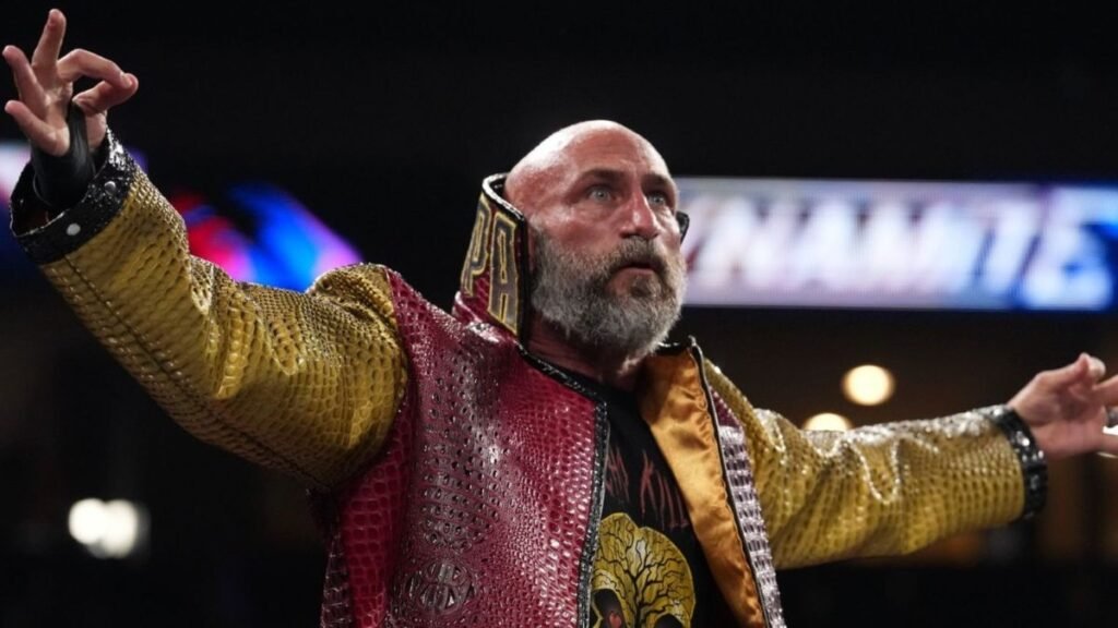 Tommaso Ciampa raises his arms during an arena appearance while wearing a red and gold entrance jacket.
