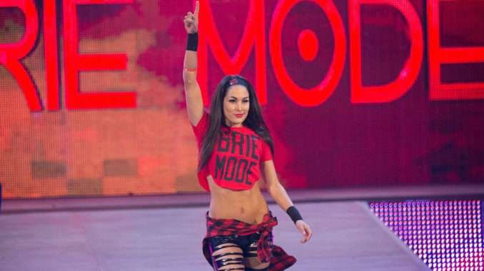 A WWE Hall of Fame women’s superstar raises her arm during a Royal Rumble entrance in Riyadh, wearing red ring gear with “Brie Mode” displayed on the stage screen behind her.
