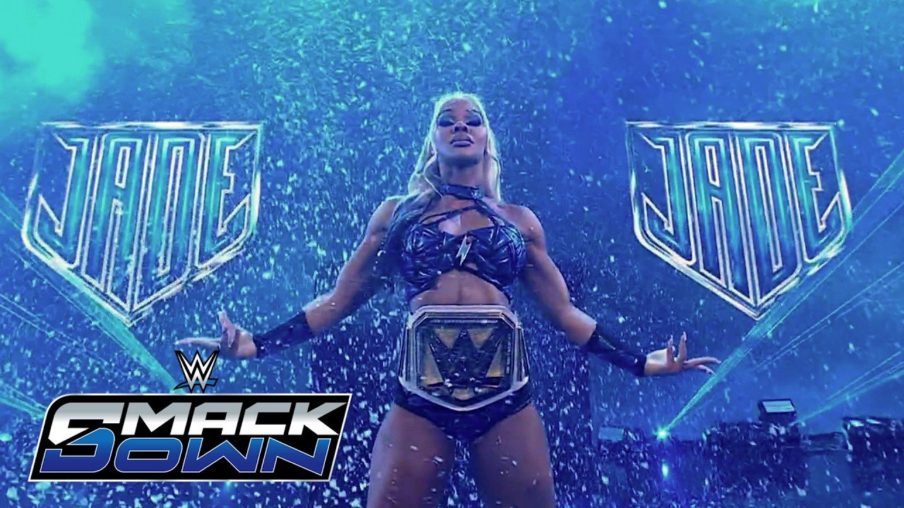 Professional wrestler Jade Cargill stands in the center of the WWE SmackDown entrance ramp, wearing a dark blue sequined ring outfit and the WWE Women's Championship belt, flanked by two large neon-blue shields displaying her name.