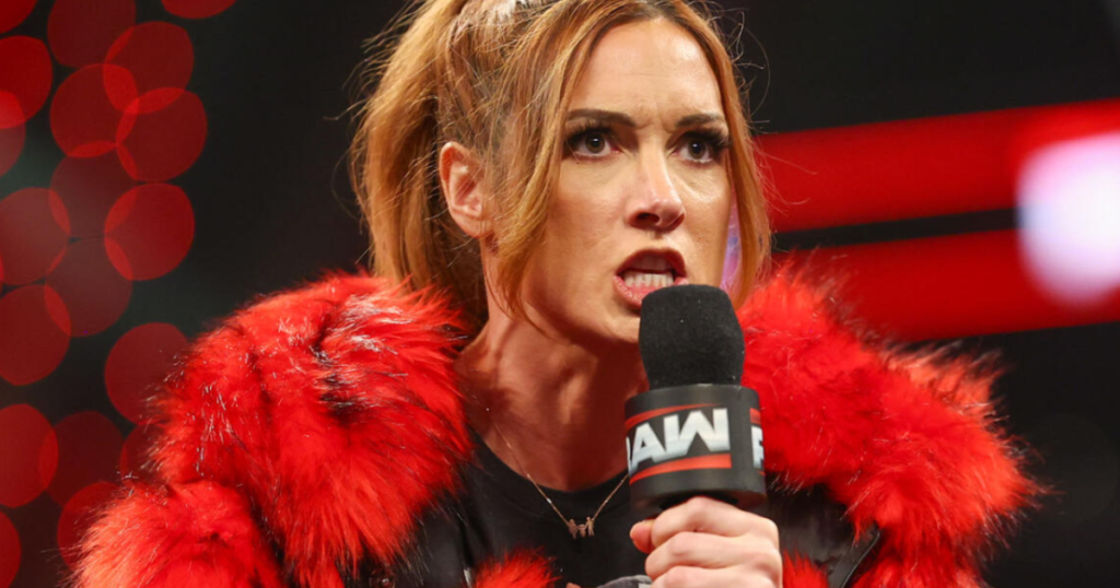 Becky lynch protests "injustice" on wwe raw - tjr wrestling Wwe superstar becky lynch wears a vibrant red faux-fur coat while speaking into a wwe raw-branded microphone. She has a fierce, focused expression with her mouth open as if delivering an intense promo. Her signature auburn hair is styled in a high ponytail, and she is wearing a thin gold necklace.