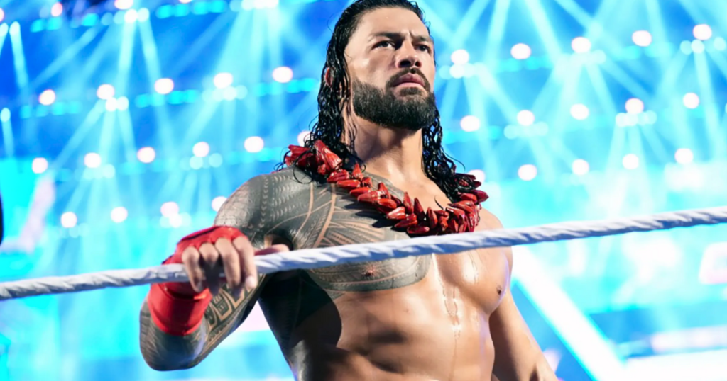 Roman reigns stands inside the ring under bright arena lights, wearing a red lei and looking focused ahead. - tjr wrestling