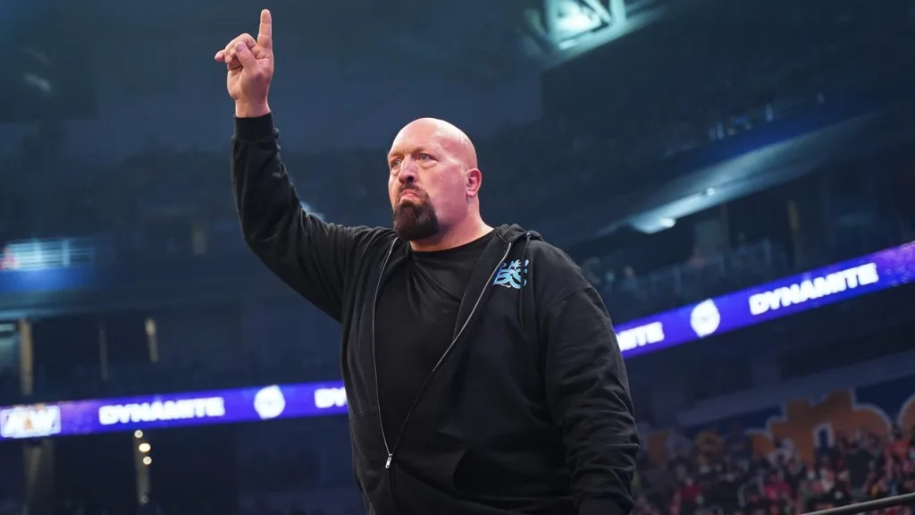 A veteran professional wrestler stands inside an aew ring, raising one finger while looking serious as arena lights shine overhead. - tjr wrestling