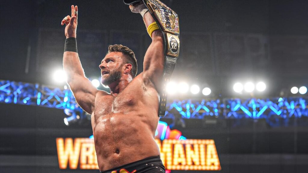 La knight raises a championship belt overhead inside a brightly lit arena, celebrating in front of a large wrestlemania stage backdrop.