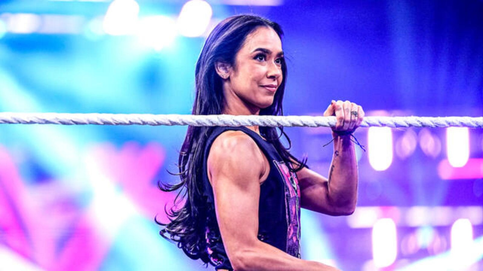 Aj lee stands inside a wwe ring, holding the top rope while looking confidently toward the crowd under bright arena lights. - tjr wrestling