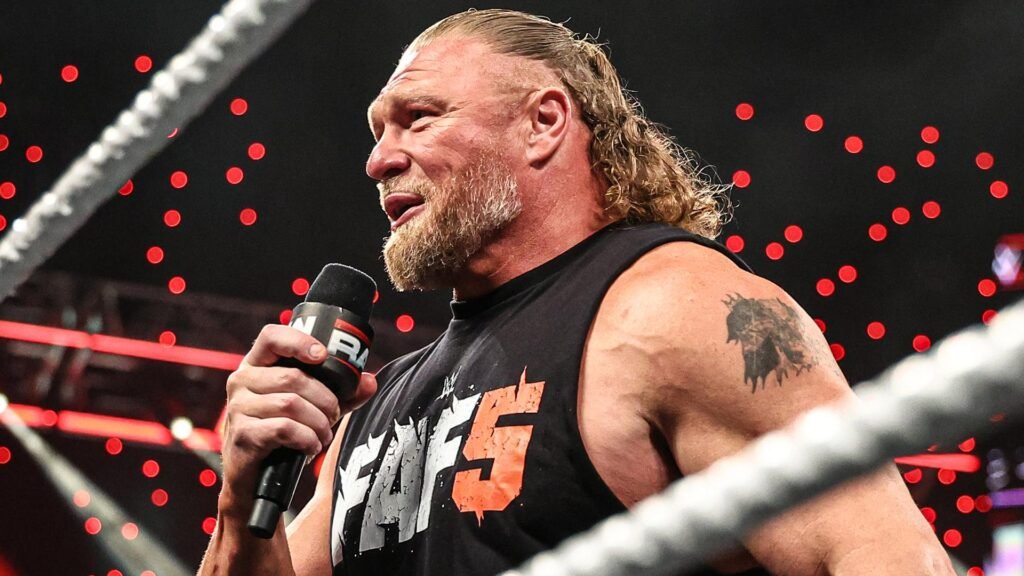 Brock lesnar addresses the crowd on wwe raw - tjr wrestling Side profile of professional wrestler brock lesnar in the ring holding a wwe raw microphone, wearing a black sleeveless shirt and sporting a ponytail and beard, against a background of red stadium lights.
