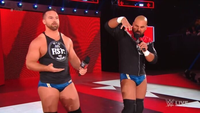 Cash Wheeler and Dax Harwood of tag team FTR standing on the WWE Raw entrance ramp, both holding microphones, with Cash wearing a black 