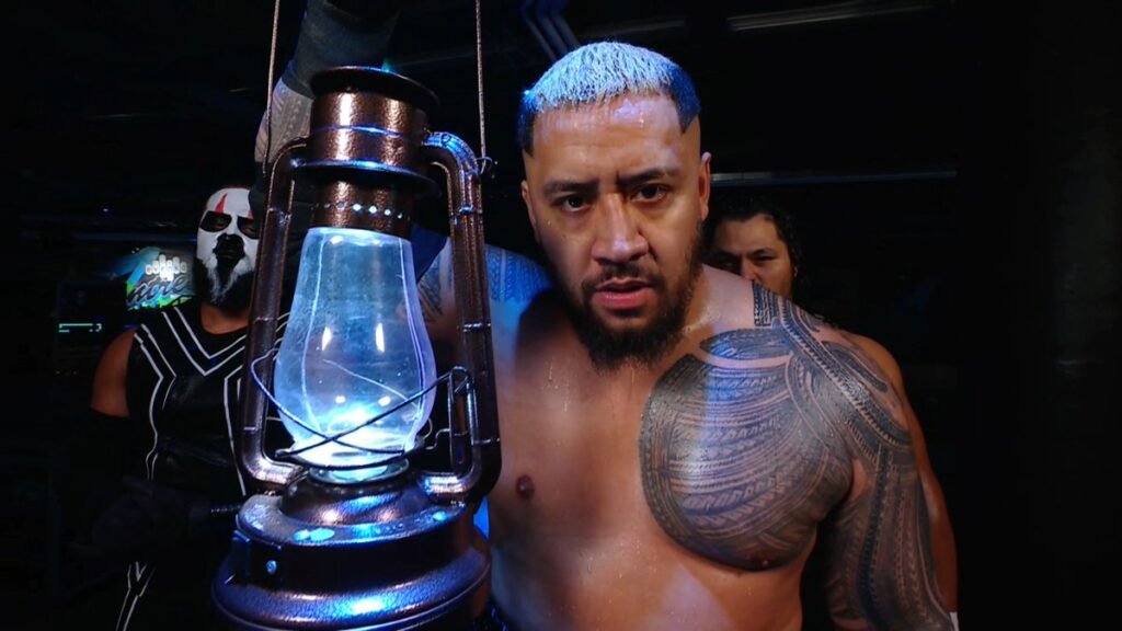 Solo sikoa appears backstage on wwe programming holding a glowing lantern while staring intensely ahead, with members of the bloodline standing behind him. - tjr wrestling