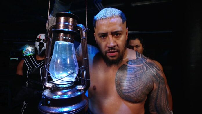 Solo Sikoa appears backstage on WWE programming holding a glowing lantern while staring intensely ahead, with members of The Bloodline standing behind him.