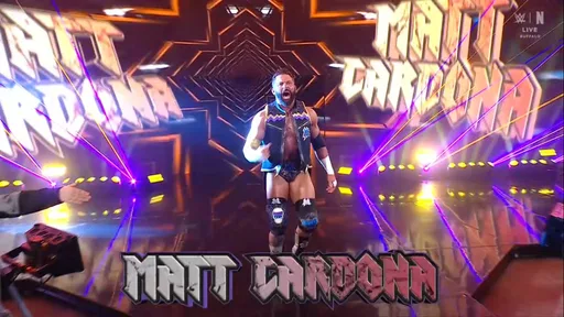 Here is the full image metadata for this wrestling entrance screenshot: alt text: wwe wrestler matt cardona making a dramatic arena entrance with his name displayed in large bold graphics on screen, surrounded by bright orange and purple laser lights in a darkened arena. - tjr wrestling