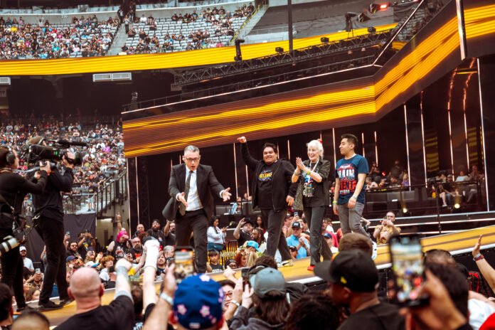 Fans and special guests walk down the entrance ramp during a WWE event inside a packed stadium.