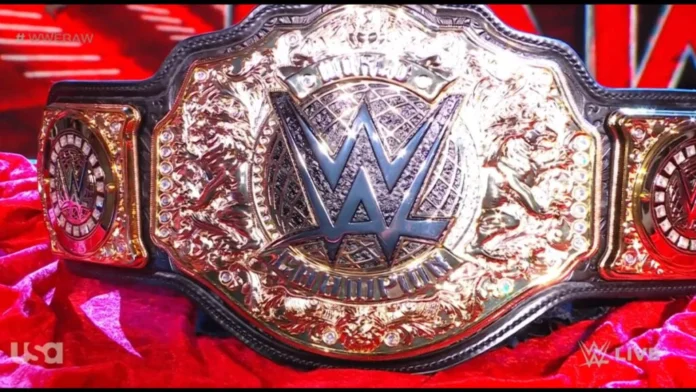 Close-up of the WWE World Heavyweight Championship belt resting on red velvet fabric, featuring a intricate gold plate with the iconic WWE logo surrounded by jewels and detailed engravings.