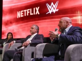 Why WWE Streaming Costs Are Surging On Netflix In Europe WWE Chief Content Officer Triple H speaks into a microphone sitting next to WWE President Nick Khan and Netflix Chief Content Officer Bela Bajaria on stage.
