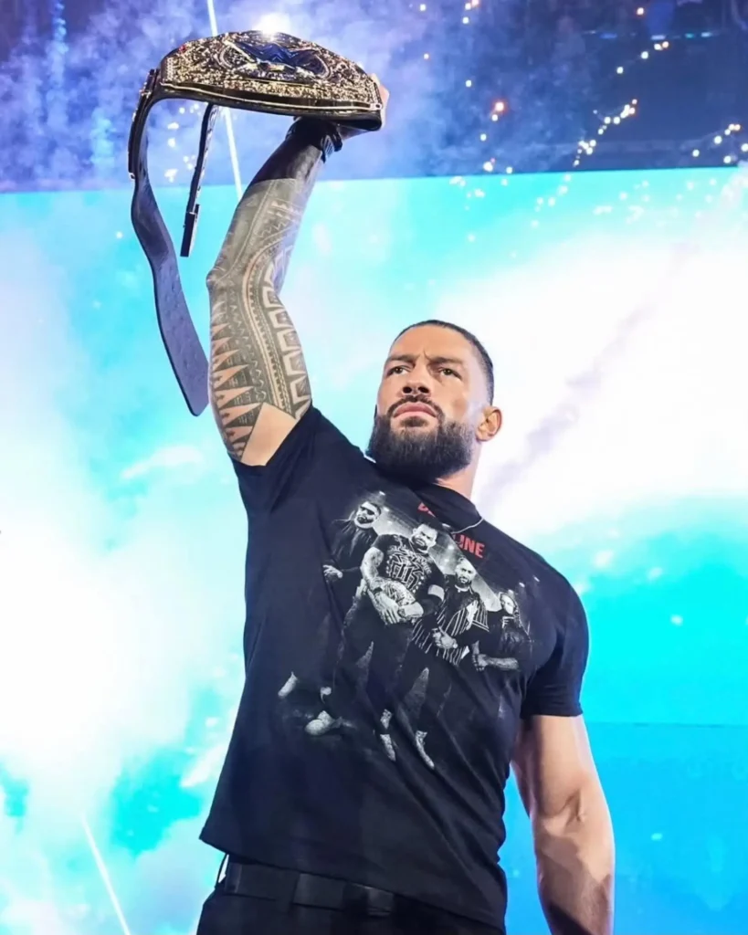 World heavyweight champion roman reigns holding his title belt high overhead during a live wwe appearance